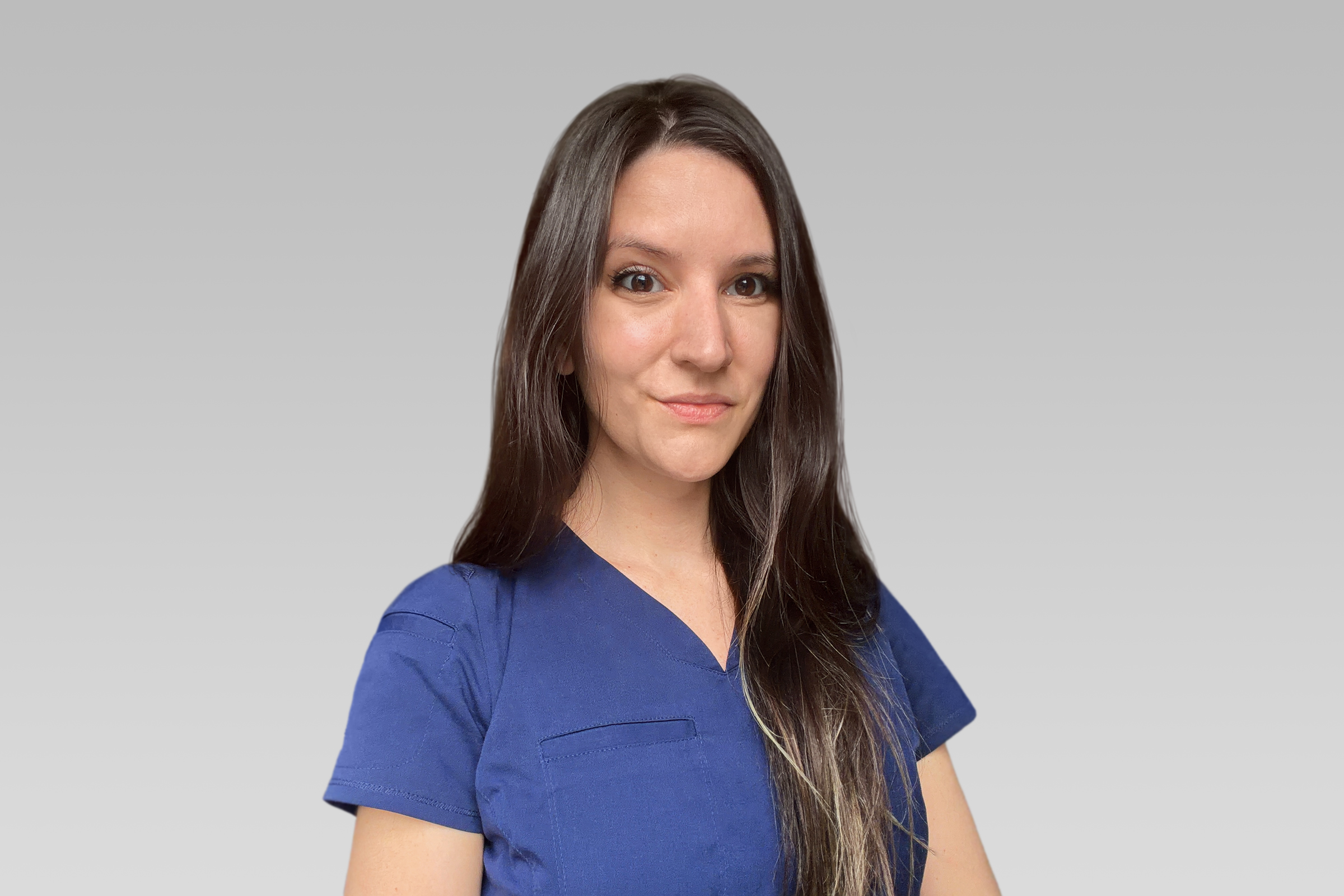 Portrait of a woman in blue scrubs, facing slightly to the right, with a subtle smile against a gray gradient background.