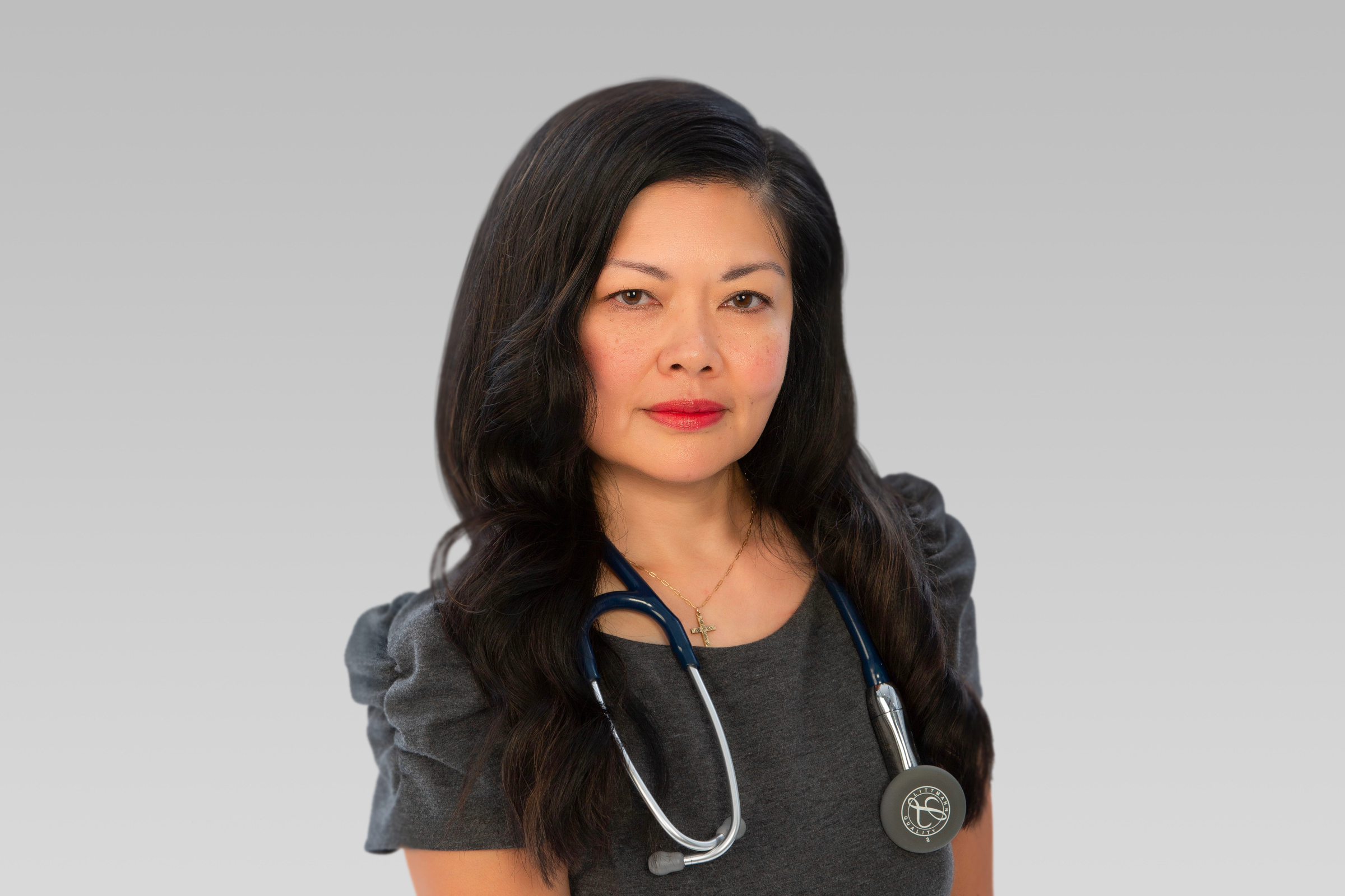 Portrait of a female healthcare professional with a stethoscope around her neck, facing the camera in a neutral setting.
