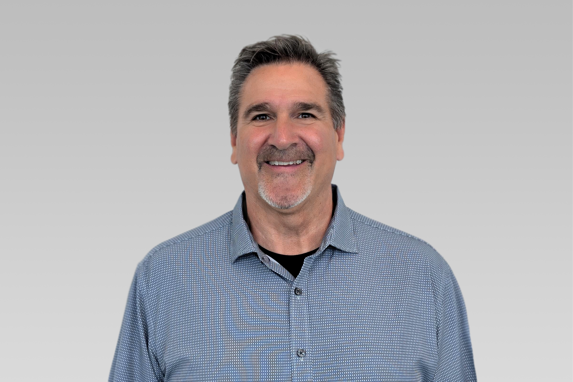 Smiling middle-aged man in a blue checkered shirt against a light gray gradient backdrop.